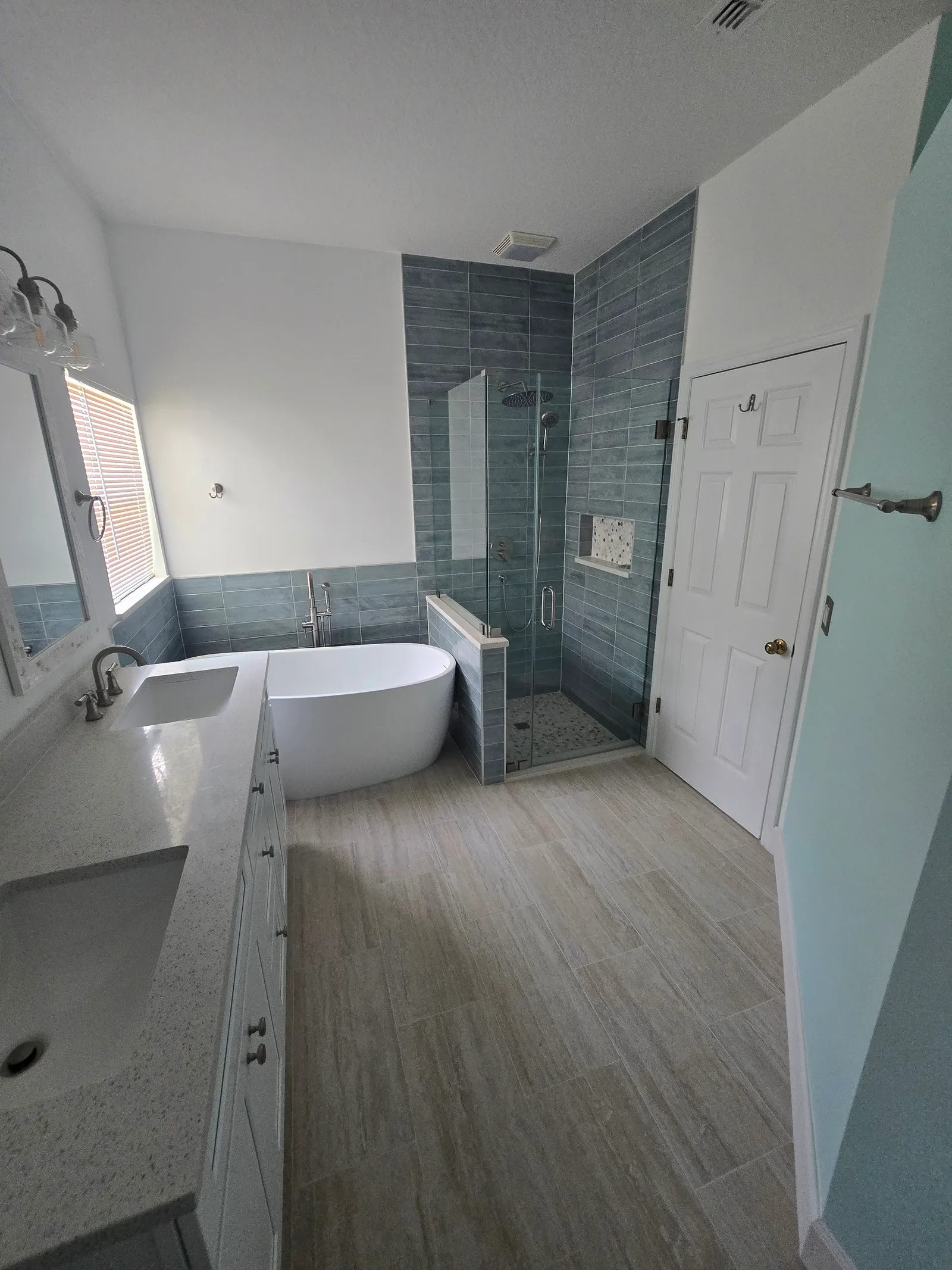 Remodeled master bath from the same spot: new white vanity, freestanding tub and frameless glass shower in grey plank-look tile