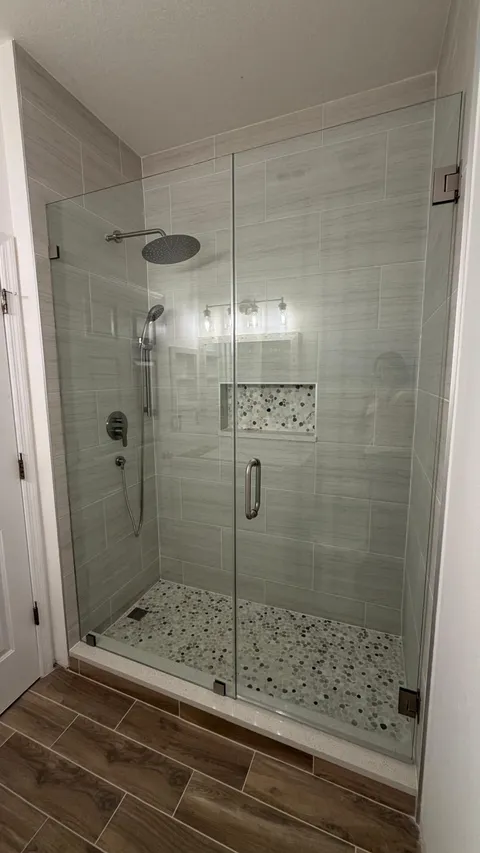 Walk-in shower with frameless glass door, light stone-look tile and pebble floor