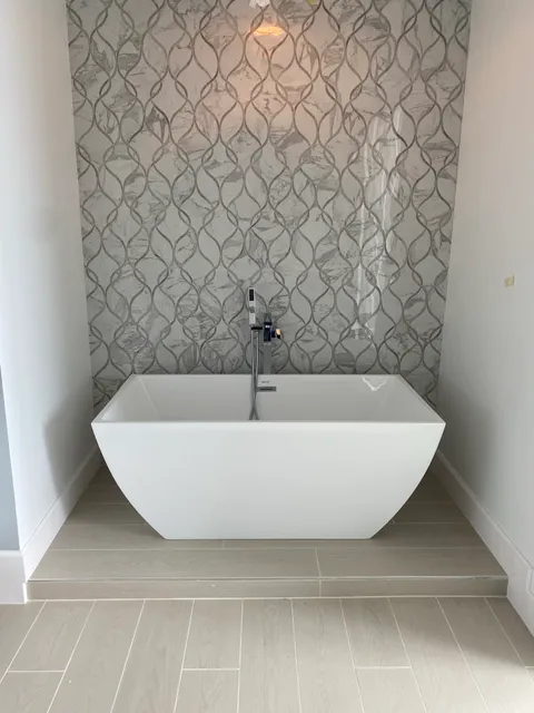 Freestanding tub on a tiled step in front of a marble-look wave tile accent wall