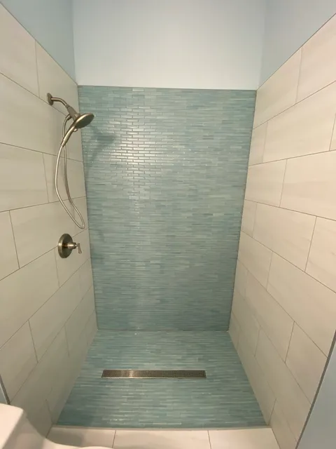 Walk-in shower with aqua glass mosaic back wall and floor, linear drain and large-format side walls