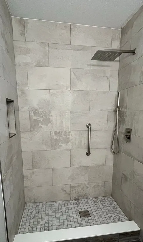 Walk-in shower with large-format stone-look tile, grab bar, niche and square rain head