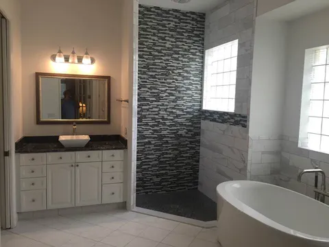 Master bath with corner walk-in shower in linear mosaic, freestanding tub and white vanity