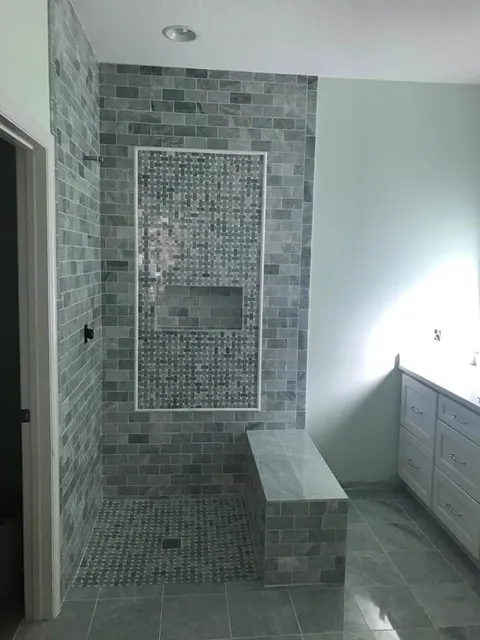 Open walk-in shower in grey marble subway tile with basketweave mosaic panel, niche and bench