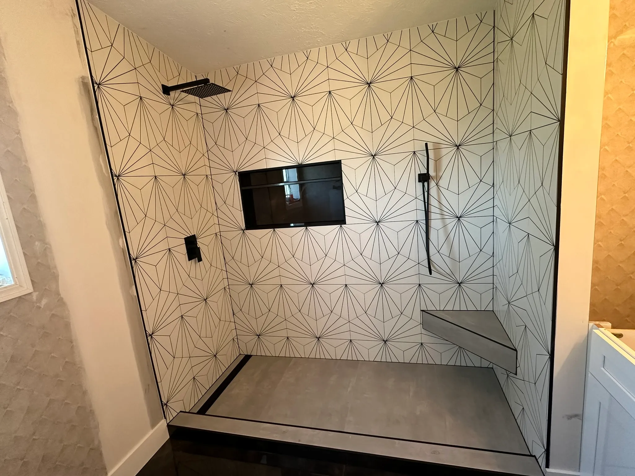 Shower rebuild with geometric patterned tile, dark floor and black fixtures