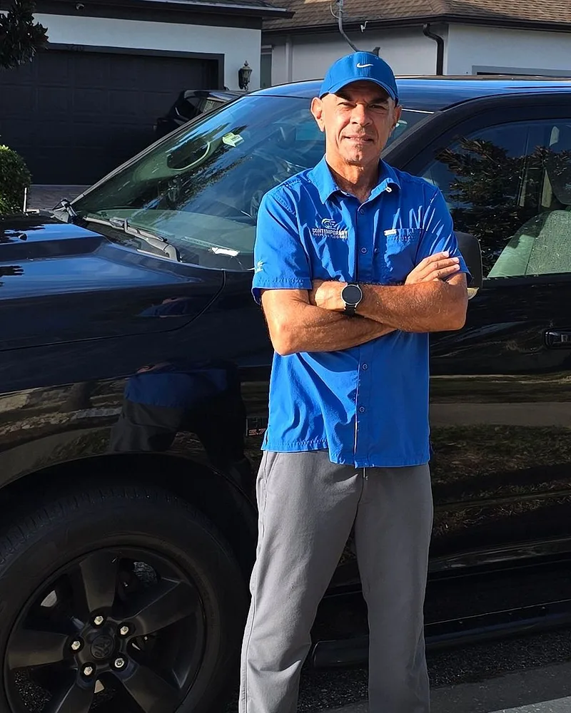 Renato Lessa in the blue Contemporary uniform shirt, arms crossed, standing beside his work truck