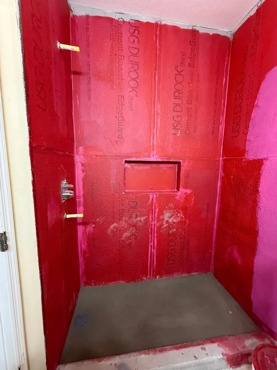 Guest shower framed and coated in red waterproofing membrane with the niche cut in