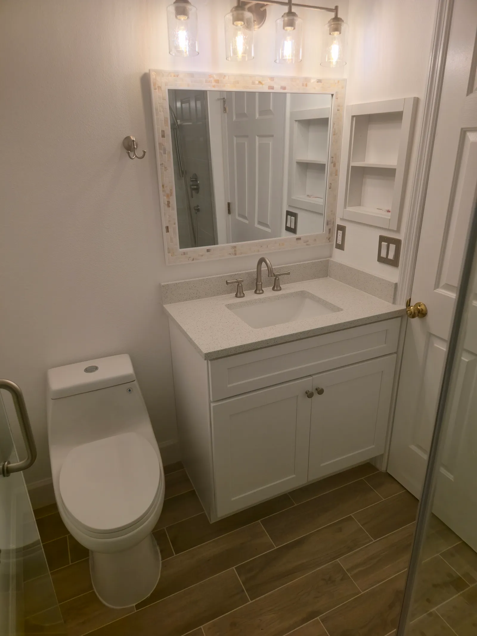 Finished guest bath with new white vanity, framed mirror, sconces and plank-look floor tile