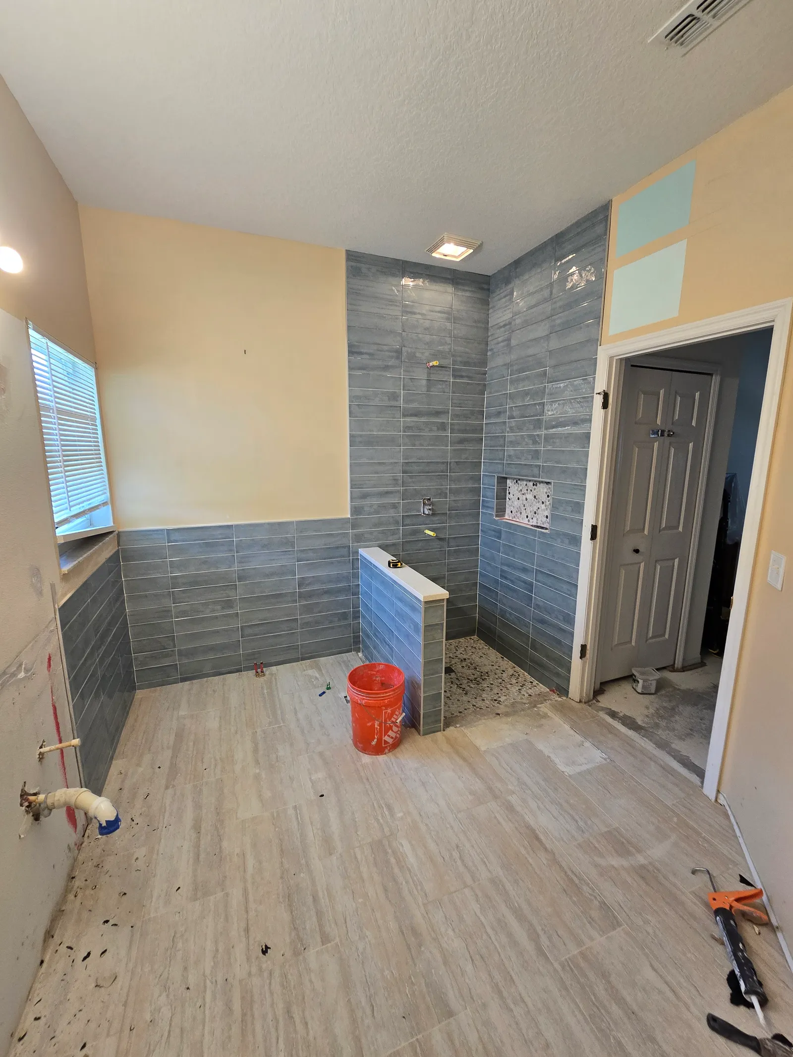 Grey plank-look tile finished on the shower walls and half wall, floor tile down, fixtures not yet installed